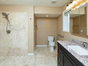 Bathroom with tile patterned flooring, tiled shower, vanity, a textured ceiling, and toilet