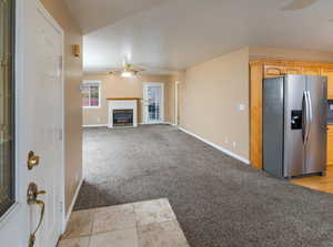 Unfurnished living room featuring light carpet, a tiled fireplace, and ceiling fan