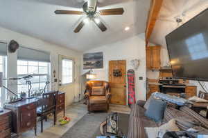 Living room with vaulted ceiling with beams, light laminate floors, and ceiling fan.