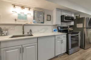 Kitchen featuring white cabinetry, sink, stainless steel appliances, and laminate flooring.  Custom quartz top & 14' quartz backsplash with shelf.