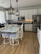 Kitchen featuring appliances with stainless steel finishes, hanging light fixtures, and white cabinets, Black granite and hardwood flooring.