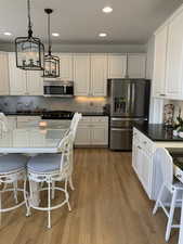 Kitchen with pendant lighting, white cabinets, and appliances with stainless steel finishes.  Black granite and hardwood flooring.