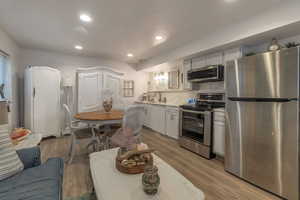 Kitchen with stainless steel appliances, sink, white cabinets, and laminate flooring.  Quartz countertops & backsplash.