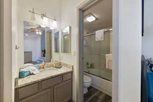 Full bathroom with hardwood / wood-style flooring, enclosed tub / shower combo, vanity, and toilet