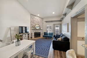 Living room featuring hardwood / wood-style flooring, a stone fireplace, and lofted ceiling