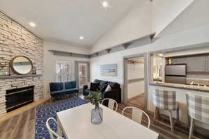 Dining room with a stone fireplace, dark wood-type flooring, and high vaulted ceiling