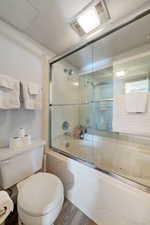 Bathroom with enclosed tub / shower combo, toilet, and hardwood / wood-style floors