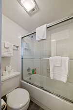 Bathroom featuring enclosed tub / shower combo, hardwood / wood-style floors, a textured ceiling, and toilet