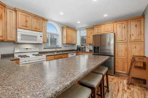 Kitchen featuring a kitchen breakfast bar, sink, light brown cabinetry, and white appliances