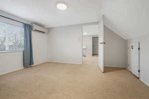 Interior space featuring lofted ceiling, a wall mounted air conditioner, and light carpet