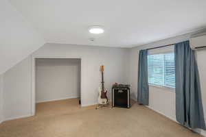 Interior space featuring a wall mounted air conditioner, lofted ceiling, and light carpet