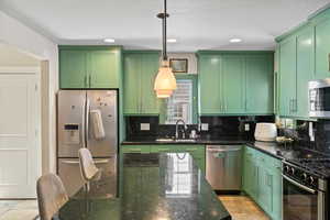 Kitchen with sink, dark stone countertops, hanging light fixtures, green cabinets, and stainless steel appliances