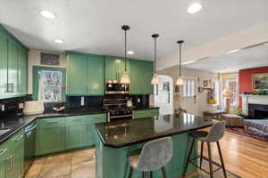 Kitchen with pendant lighting, green cabinets, appliances with stainless steel finishes, a kitchen island, and decorative backsplash