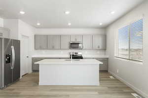 Kitchen featuring appliances with stainless steel finishes, gray cabinets, a sink, a kitchen island with sink, and light countertops
