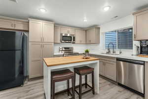 Kitchen featuring sink, appliances with stainless steel finishes, butcher block counters, a kitchen island, and a kitchen bar