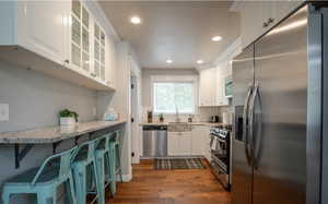 Kitchen featuring stainless steel appliances, white cabinetry, light stone countertops, and sink