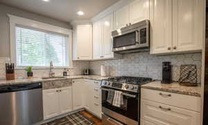 Kitchen featuring white cabinetry, sink, light stone counters, and appliances with stainless steel finishes