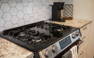 Interior details featuring tasteful backsplash, stainless steel range with gas cooktop, and stone countertops