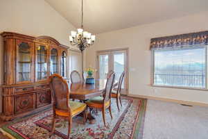 Carpeted formal dining area featuring high vaulted ceiling and an inviting chandelier