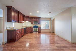 Kitchen with sink, light hardwood / wood-style flooring, a textured ceiling, appliances with stainless steel finishes, and light stone countertops