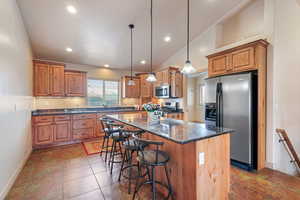 Kitchen featuring a kitchen island, sink, dark stone counters, hanging light fixtures, and stainless steel appliances