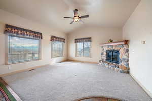 Spacious living room featuring a stone fireplace, lofted ceiling, carpeted flooring, ceiling fan, and beautiful mountain views!