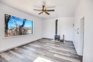 Unfurnished living room featuring wood-type flooring, ceiling fan, and a wood stove