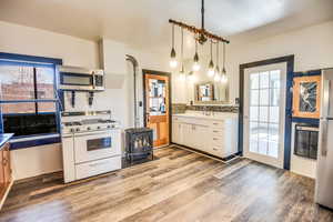 Kitchen with hanging light fixtures, appliances with stainless steel finishes, white cabinets, light hardwood / wood-style floors, and backsplash