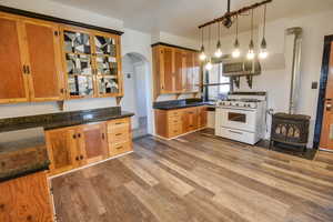 Kitchen featuring decorative light fixtures, a wood stove, dark stone counters, hardwood / wood-style flooring, and white range with gas stovetop