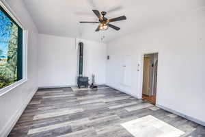 Empty room featuring hardwood / wood-style flooring, ceiling fan, and a wood stove