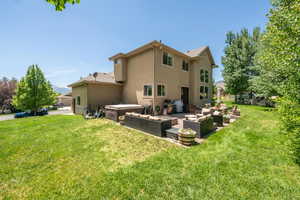 Back of house featuring a jacuzzi, a lawn, outdoor lounge area, and a patio