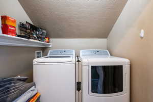 Clothes washing area featuring separate washer and dryer and a textured ceiling