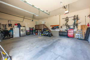 Garage with white refrigerator, a garage door opener, stainless steel fridge, and a workshop area