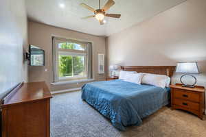 Carpeted bedroom with ceiling fan, vaulted ceiling, and a textured ceiling