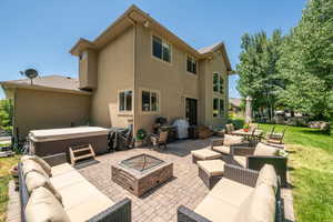 Rear view of property with a yard, an outdoor living space with a fire pit, a hot tub, and a patio