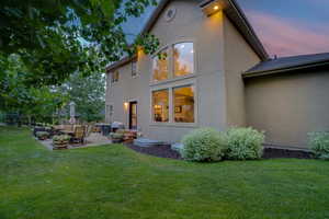 Back house at dusk with a patio area and a lawn