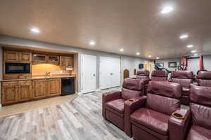 Cinema featuring indoor wet bar, light hardwood / wood-style floors, and a textured ceiling