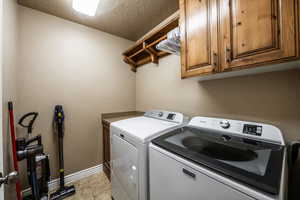 Laundry room featuring independent washer and dryer, cabinets, a textured ceiling, and light tile patterned floors