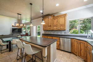 Kitchen with pendant lighting, sink, a breakfast bar area, decorative backsplash, and stainless steel dishwasher