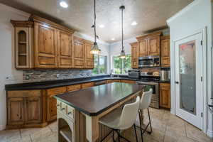 Kitchen with decorative backsplash, hanging light fixtures, ornamental molding, a center island, and stainless steel appliances