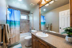 Full bathroom featuring vanity, toilet, shower / bath combo, tile patterned floors, and a textured ceiling