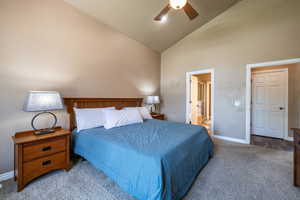 Carpeted bedroom featuring ceiling fan, ensuite bath, and high vaulted ceiling