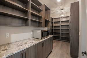 Interior space with light stone counters, decorative light fixtures, light hardwood / wood-style flooring, and dark brown cabinets