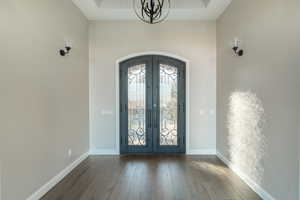 Entrance foyer with french doors, a tray ceiling, a chandelier, and hardwood / wood-style flooring