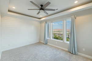 Carpeted empty room featuring ceiling fan and a raised ceiling