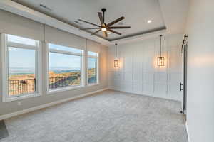 Carpeted empty room featuring a mountain view, a barn door, ceiling fan, and a tray ceiling