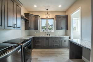 Kitchen featuring sink, dark brown cabinets, pendant lighting, light stone countertops, and washing machine and dryer