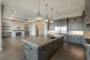 Kitchen with sink, a kitchen island with sink, high end appliances, decorative light fixtures, and a raised ceiling