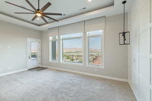 Carpeted empty room with a tray ceiling, ceiling fan, and a high ceiling