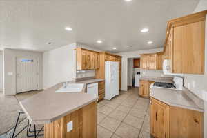 Kitchen featuring washer / clothes dryer, sink, a kitchen bar, white appliances, and a textured ceiling